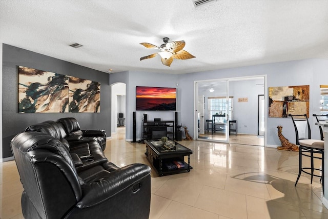 living room with ceiling fan, a textured ceiling, and light tile patterned flooring