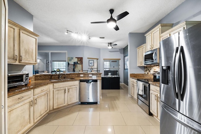 kitchen featuring kitchen peninsula, appliances with stainless steel finishes, dark stone countertops, a textured ceiling, and sink