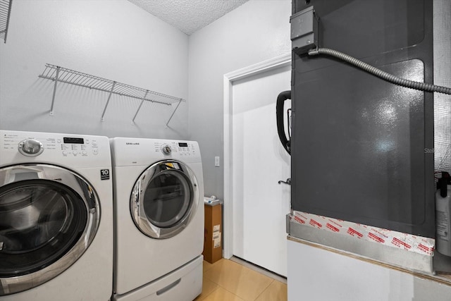 clothes washing area with a textured ceiling, light tile patterned floors, and washing machine and dryer