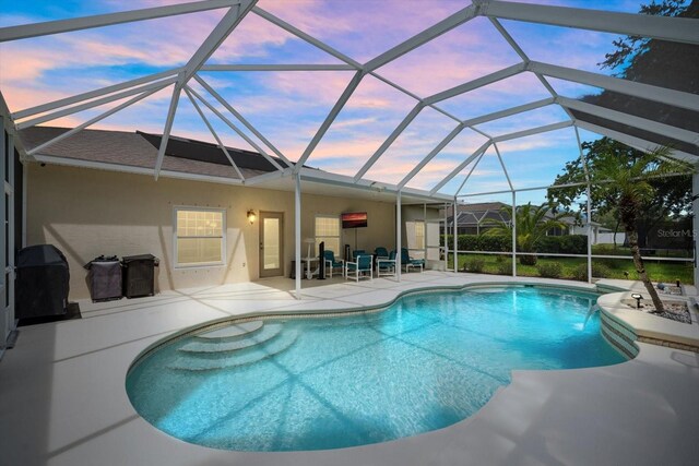 pool at dusk featuring a lanai and a patio