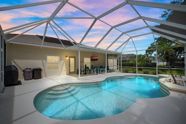 pool at dusk featuring glass enclosure, a patio area, and grilling area