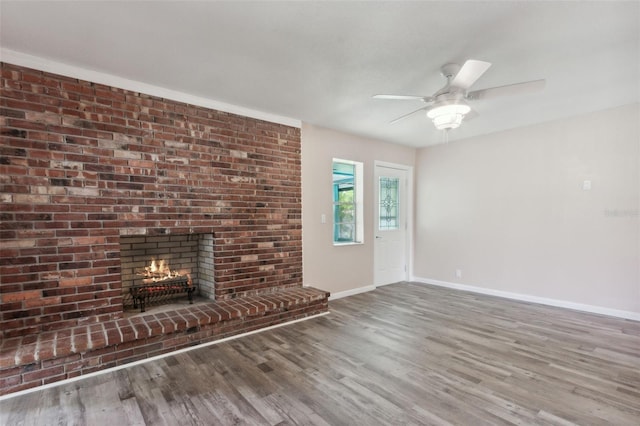 unfurnished living room with wood-type flooring, a brick fireplace, and ceiling fan