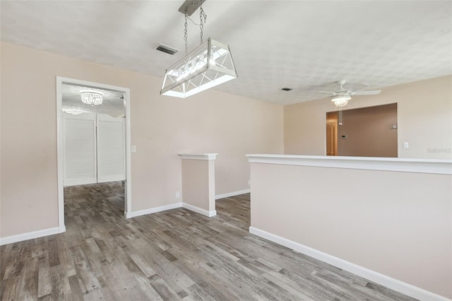 empty room featuring ceiling fan with notable chandelier and hardwood / wood-style floors