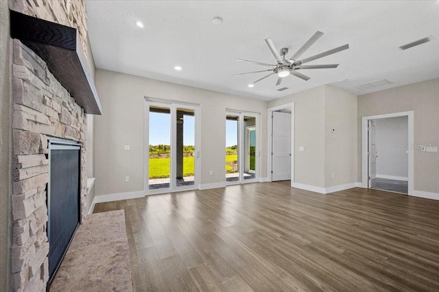 unfurnished living room with ceiling fan, wood-type flooring, and a stone fireplace