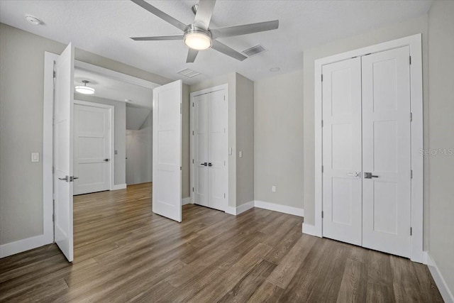 unfurnished bedroom with multiple closets, dark hardwood / wood-style floors, and ceiling fan