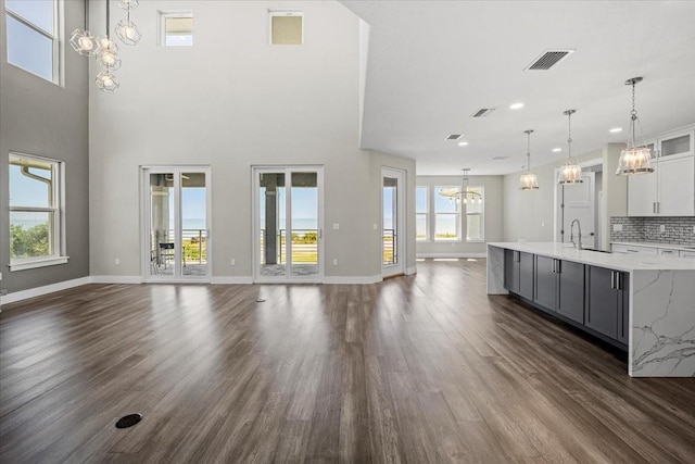 unfurnished living room with a towering ceiling, dark hardwood / wood-style flooring, a chandelier, and sink