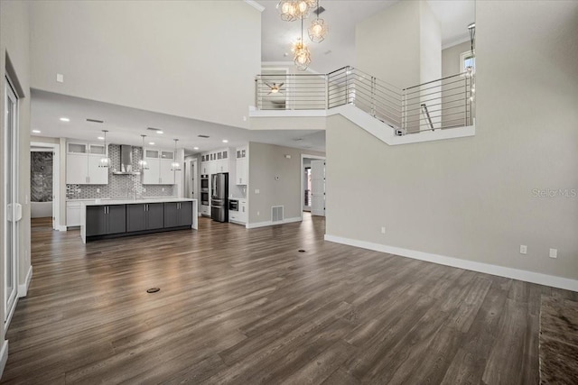 unfurnished living room with an inviting chandelier, a towering ceiling, and dark hardwood / wood-style floors