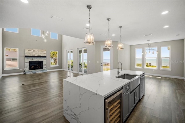 kitchen with wine cooler, hanging light fixtures, a center island with sink, a fireplace, and light stone countertops