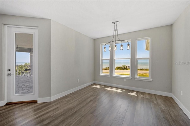 unfurnished dining area featuring an inviting chandelier, dark hardwood / wood-style floors, and a water view