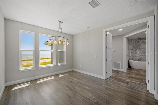 unfurnished dining area with an inviting chandelier, dark hardwood / wood-style floors, a textured ceiling, and a water view