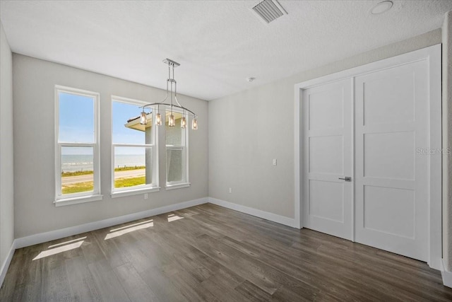 unfurnished dining area with dark hardwood / wood-style flooring, a notable chandelier, a textured ceiling, and a water view