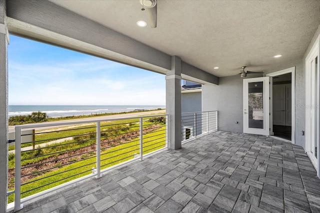 view of patio / terrace featuring a view of the beach, ceiling fan, a balcony, and a water view