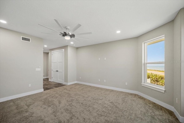 empty room with a textured ceiling, ceiling fan, and dark colored carpet