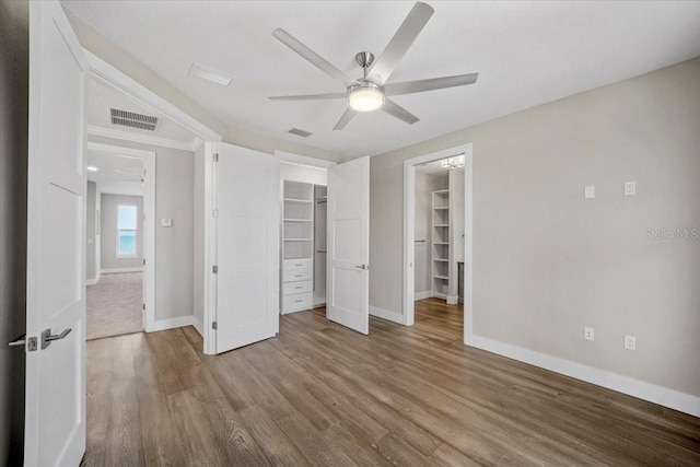 unfurnished bedroom featuring wood-type flooring, a spacious closet, ceiling fan, and a closet