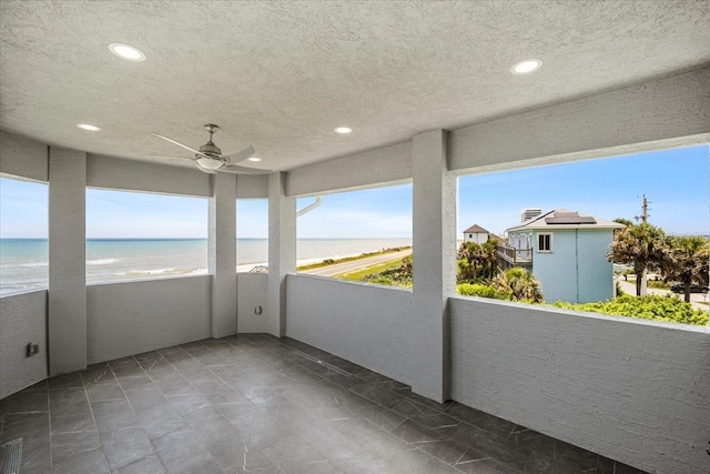 unfurnished sunroom with ceiling fan, a beach view, and a water view