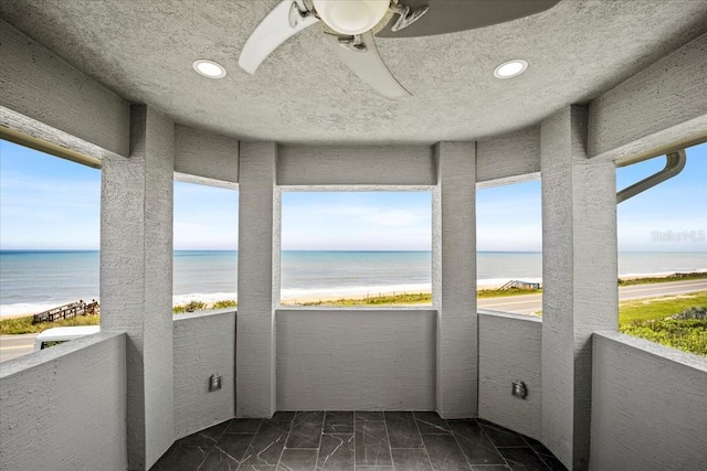 sunroom with a water view, a beach view, and ceiling fan