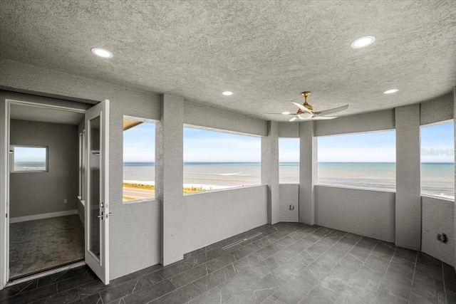 unfurnished sunroom featuring a water view, a beach view, and ceiling fan