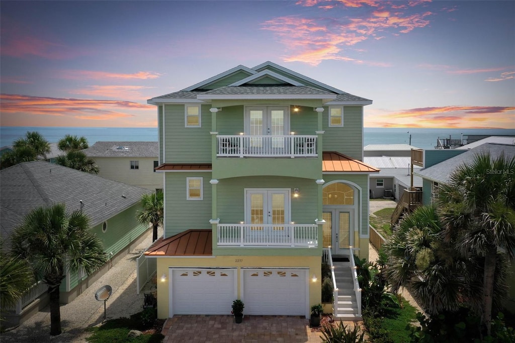 view of front facade featuring a garage, a balcony, a water view, and french doors