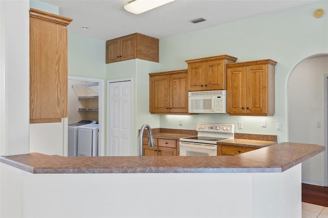 kitchen with light tile patterned flooring, washer and clothes dryer, kitchen peninsula, and white appliances