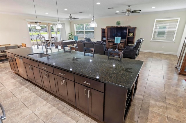 kitchen with ornamental molding, dark stone countertops, light tile patterned floors, and an island with sink