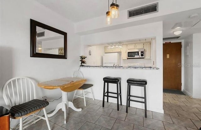 kitchen featuring white refrigerator, decorative backsplash, a kitchen bar, and decorative light fixtures