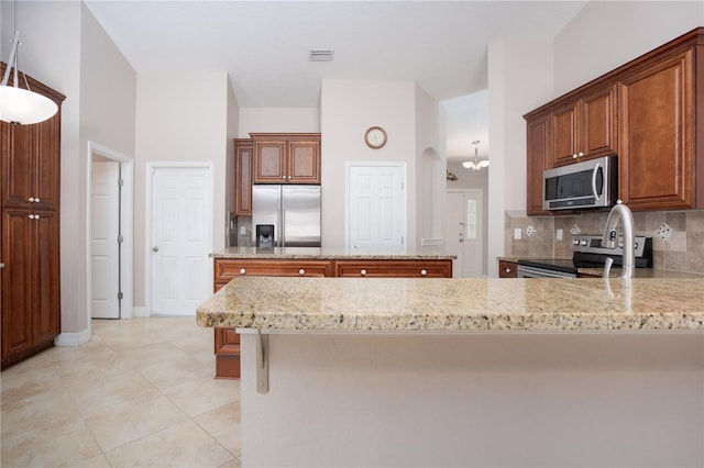 kitchen with stainless steel appliances, tasteful backsplash, light stone counters, and decorative light fixtures