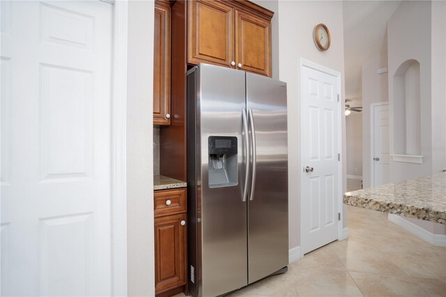 kitchen with light tile patterned floors, stainless steel fridge, light stone countertops, and ceiling fan