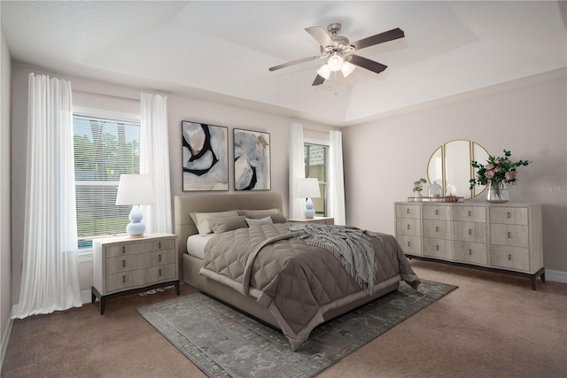 carpeted bedroom with ceiling fan and a tray ceiling