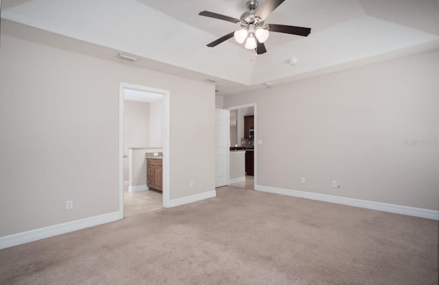 unfurnished bedroom with ceiling fan, light colored carpet, ensuite bathroom, and a raised ceiling