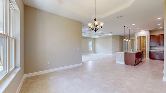 kitchen featuring light stone counters, decorative light fixtures, a notable chandelier, open floor plan, and an island with sink