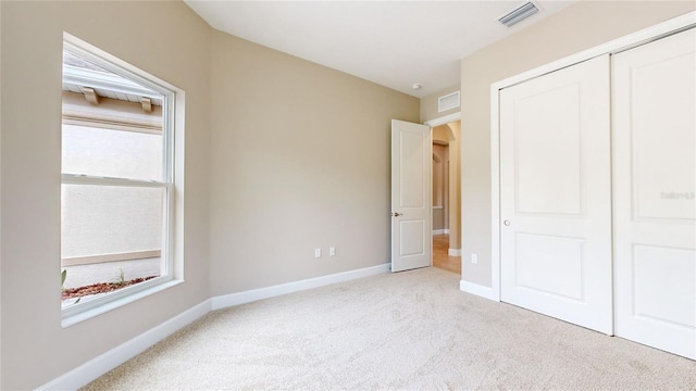 unfurnished bedroom with light colored carpet, a closet, visible vents, and baseboards