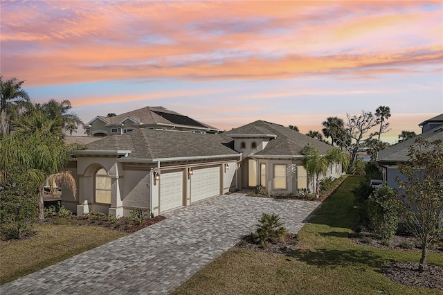 view of front facade with decorative driveway, stucco siding, a shingled roof, an attached garage, and a front lawn