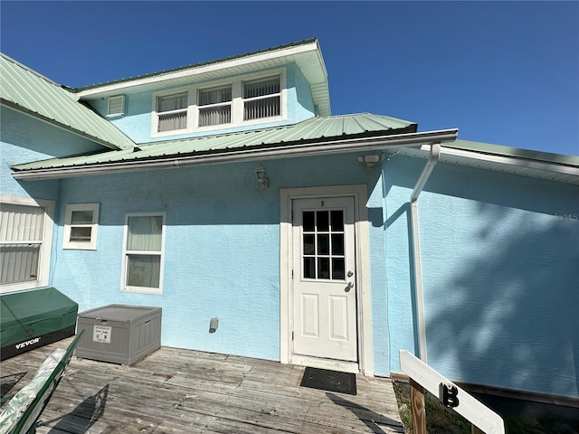 view of exterior entry featuring metal roof, a deck, and stucco siding