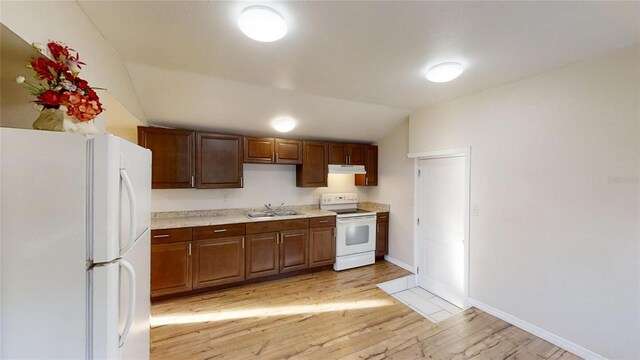 kitchen featuring lofted ceiling, under cabinet range hood, white appliances, a sink, and light countertops