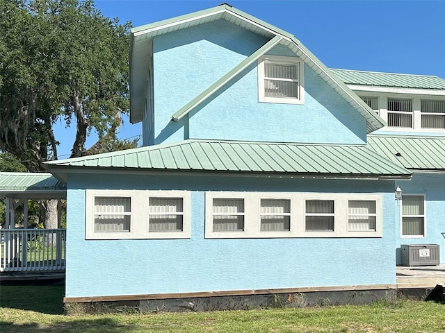 view of side of property with central air condition unit, a wooden deck, metal roof, and stucco siding