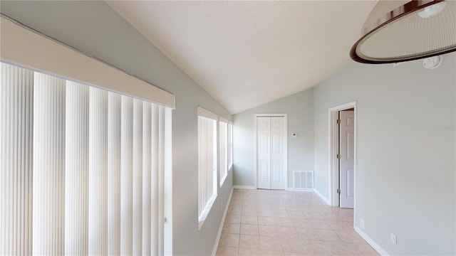 hall featuring light tile patterned floors, baseboards, visible vents, and vaulted ceiling