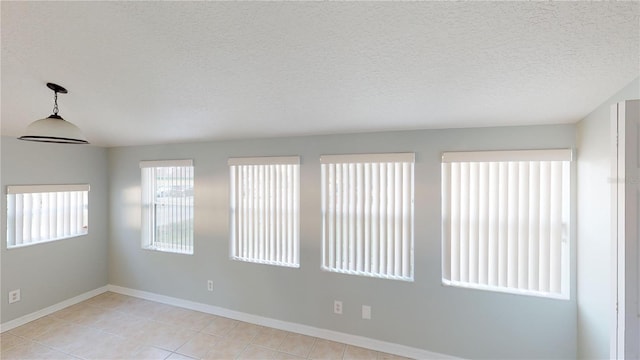 unfurnished room featuring a textured ceiling, light tile patterned flooring, and baseboards