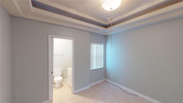 interior space with light tile patterned floors, a tray ceiling, ensuite bathroom, and baseboards