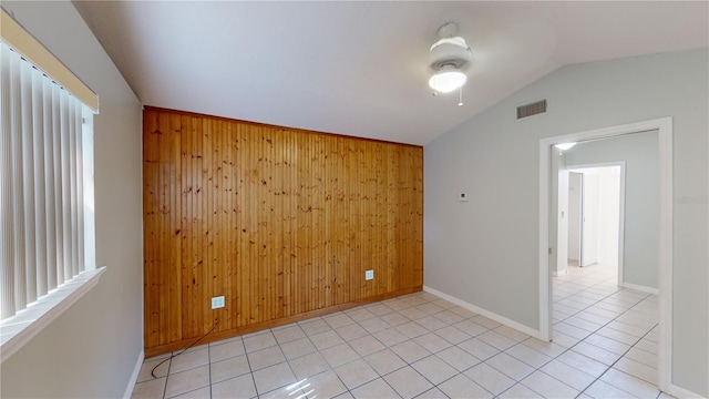 spare room featuring light tile patterned floors, baseboards, visible vents, lofted ceiling, and wood walls