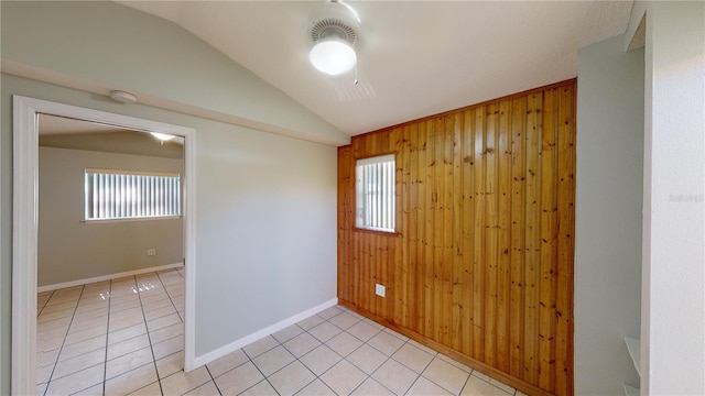 unfurnished room featuring plenty of natural light, vaulted ceiling, wooden walls, and light tile patterned floors