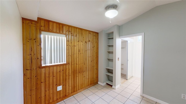 spare room with baseboards, vaulted ceiling, wood walls, built in shelves, and light tile patterned flooring