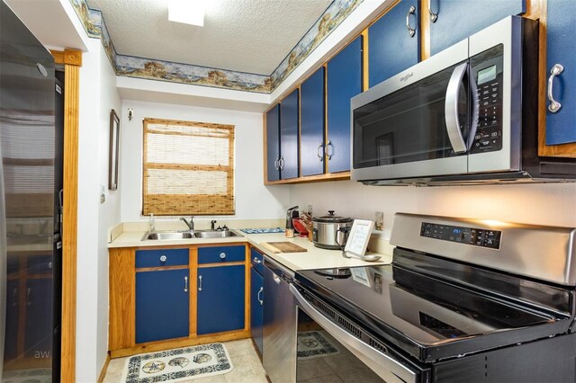 kitchen featuring light tile patterned floors, a textured ceiling, stainless steel appliances, blue cabinetry, and sink