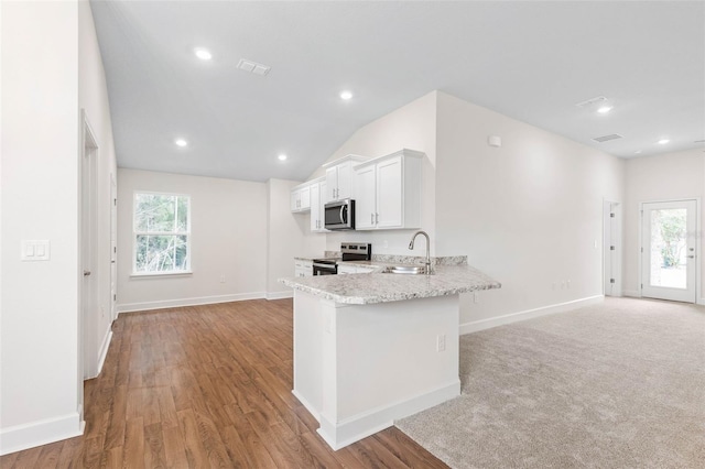 kitchen with appliances with stainless steel finishes, sink, white cabinets, kitchen peninsula, and light stone counters