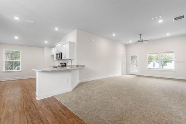 kitchen featuring light stone counters, white cabinetry, kitchen peninsula, and a healthy amount of sunlight