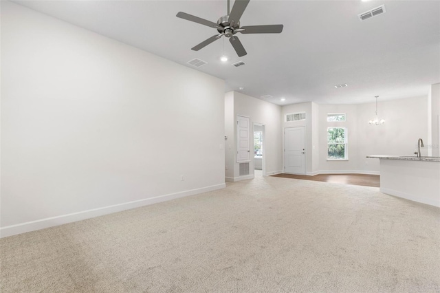 unfurnished living room featuring light carpet, sink, and ceiling fan with notable chandelier