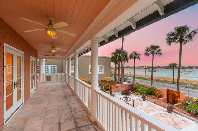 balcony at dusk featuring french doors, ceiling fan, and a water view