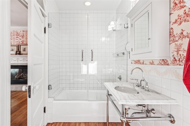 bathroom featuring hardwood / wood-style flooring, enclosed tub / shower combo, sink, and tile walls