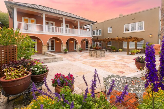 back house at dusk featuring ceiling fan, a balcony, and a patio