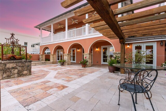 patio terrace at dusk featuring a balcony, ceiling fan, and french doors