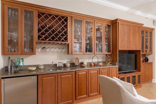 bar with refrigerator, sink, light tile patterned flooring, ornamental molding, and dark stone counters